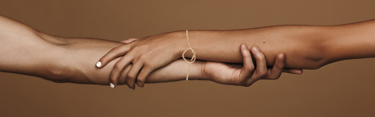 An image of two people holding each others forearms, tied with a heart string